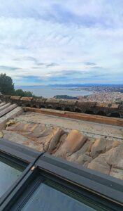 Toiture en cours de réfection, ancienne sous-couche déposée derrière une fenêtre de toit, vue sur la mer