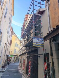 Ruelle avec échafaudage fixé contre une façade ancienne et panneau de chantier couverture charpente façade
