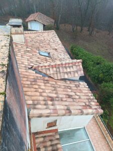 Toiture de maison en tuiles canal avec velux et lucarne, vue en plongée depuis un toit voisin