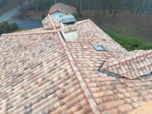 Vue plongeante d'une grande toiture à croupes en tuiles canal, souche de cheminée et noue, maison en forêt