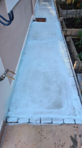 Revêtement d'étanchéité liquide gris appliqué sur une allée extérieure en béton le long d'une maison