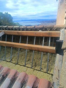 Toiture ouverte en rénovation : poutres et tiges métalliques au-dessus de l'isolant, vue sur la baie