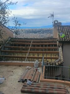 Toiture déposée avec solives en bois à nu, plaques sous-tuiles et tuiles canal stockées sur la terrasse