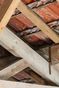 Charpente ancienne en bois vue depuis les combles, sous une couverture en tuiles mécaniques rouges