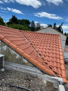 Toiture neuve en tuiles romanes rouges avec noue entre deux pans, au-dessus d'un toit gravillonné